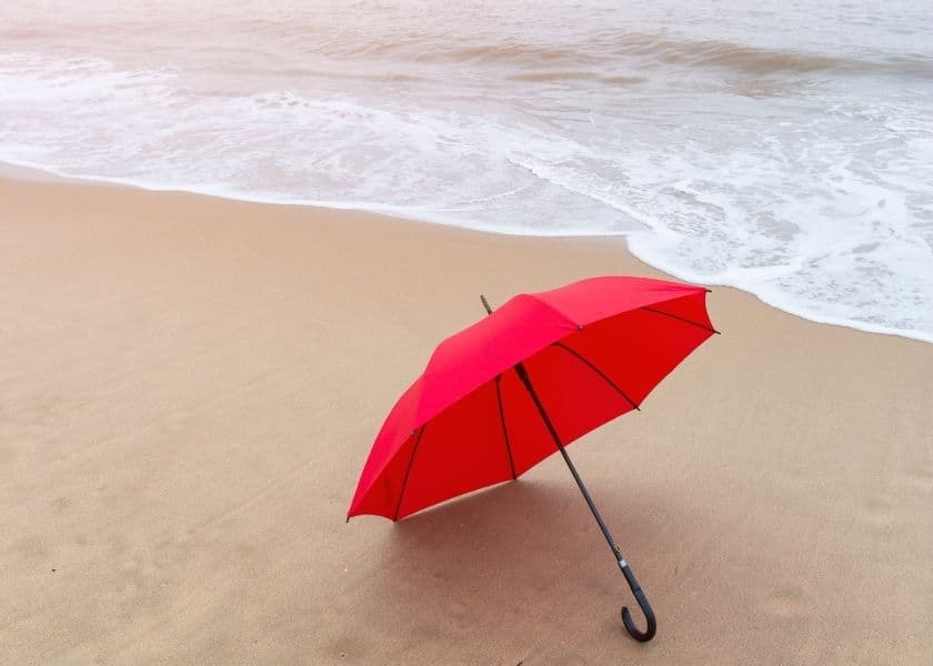 A red umbrella rests on the sandy beach near the water's edge. A red umbrella rests on the sandy beach near the water's edge.