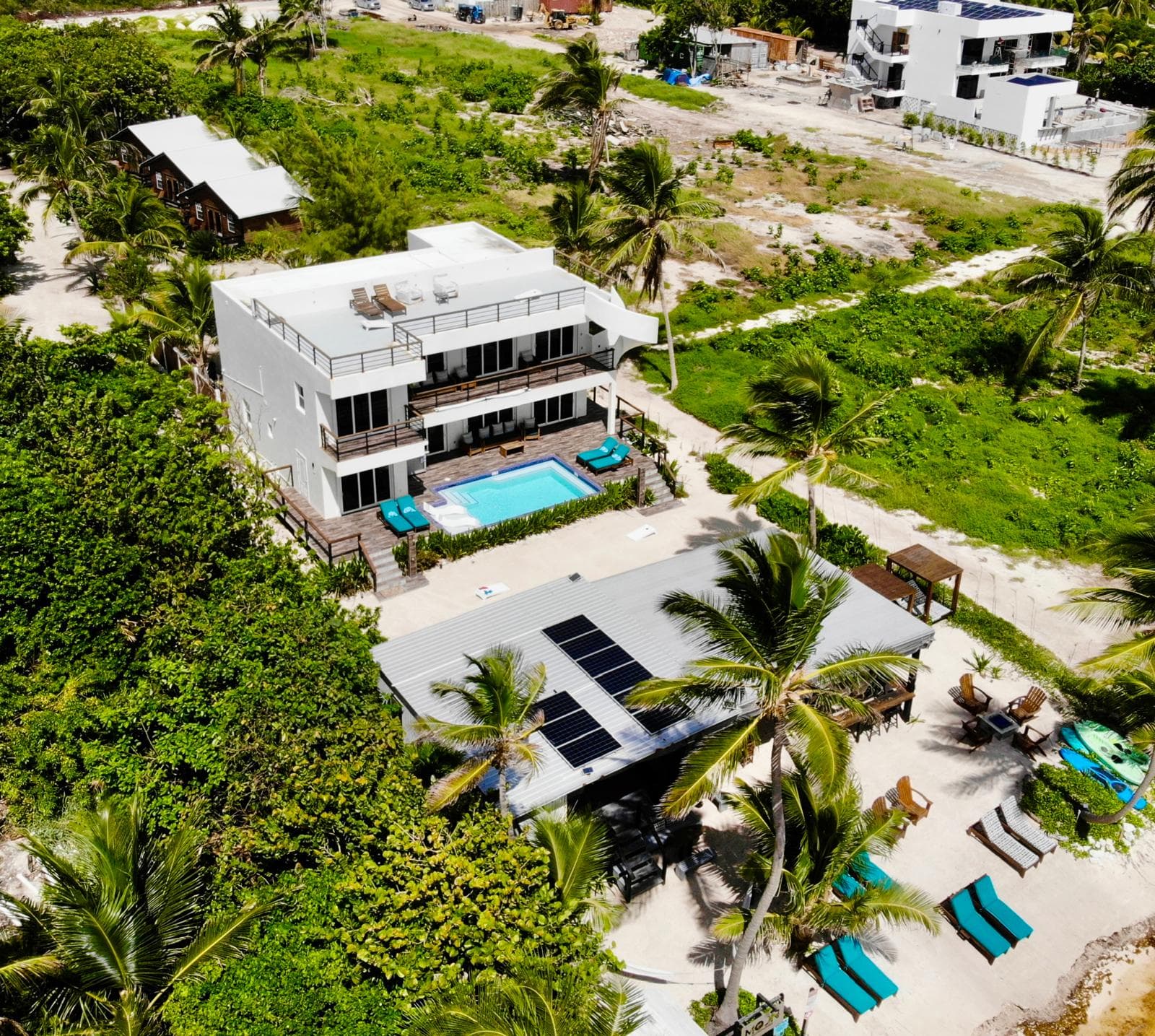 Aerial view of a modern villa with a swimming pool surrounded by palm trees and green landscaping.
