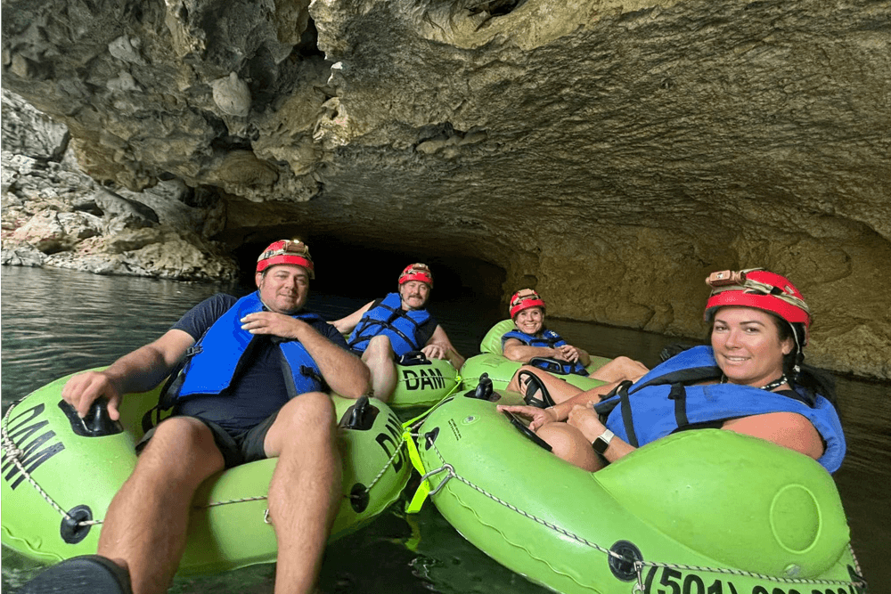 Four people in green inflatable rafts wearing helmets float in a cave.