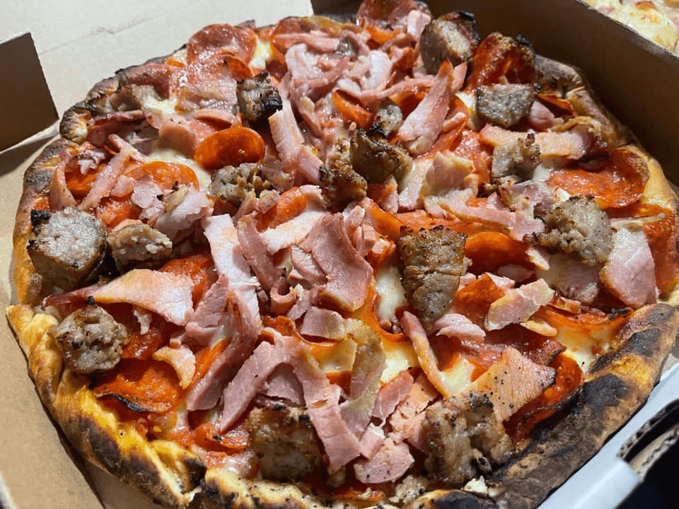 A meat lover's pizza topped with pepperoni, ham, and sausage in a pizza box.