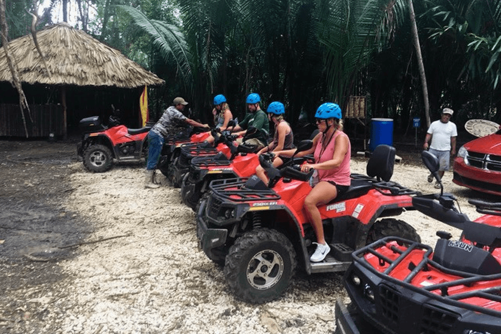Group of people wearing helmets preparing to ride ATVs in a tropical setting.