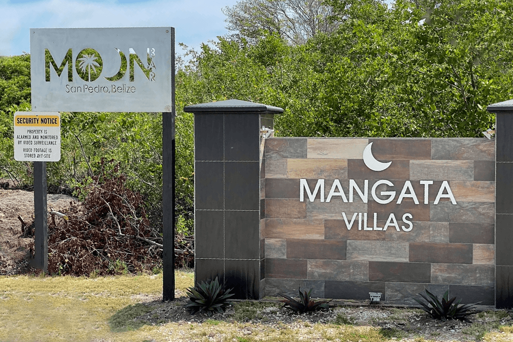 Signs for "MOON" and "MANGATA VILLAS" at a resort in San Pedro, Belize, surrounded by greenery.