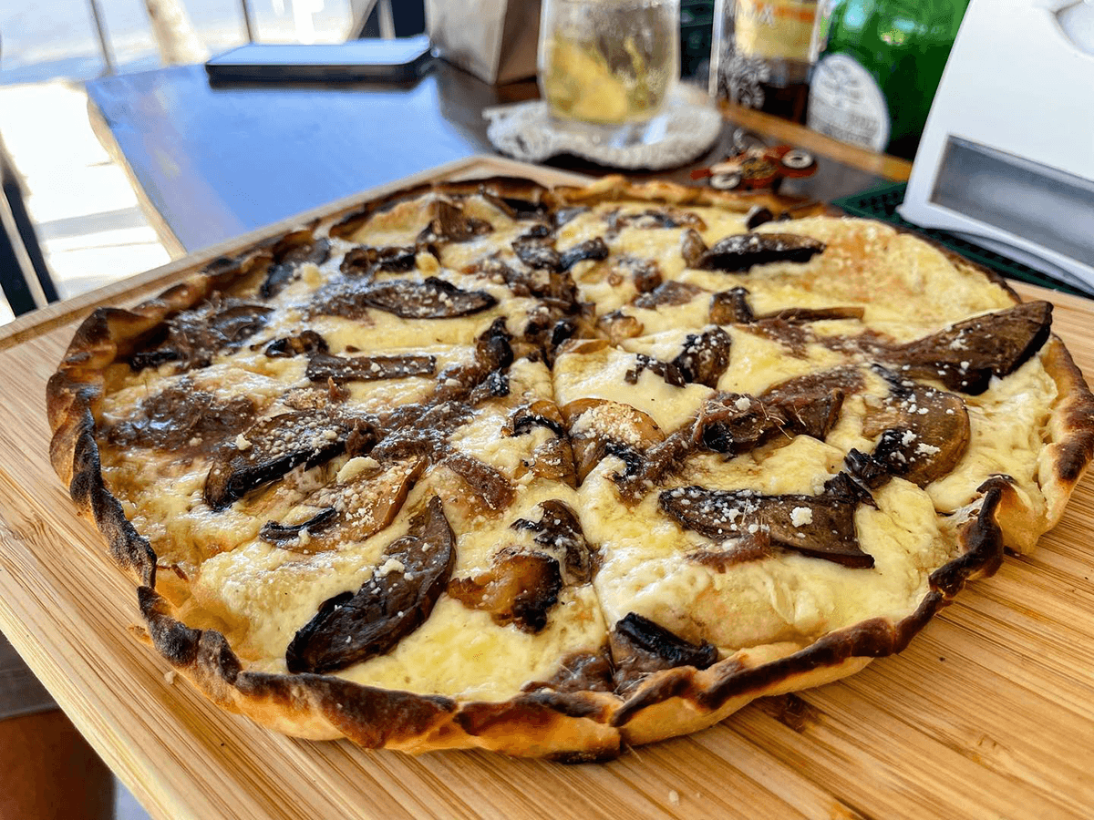 A freshly baked flatbread topped with cheese and sautéed mushrooms on a wooden serving board.