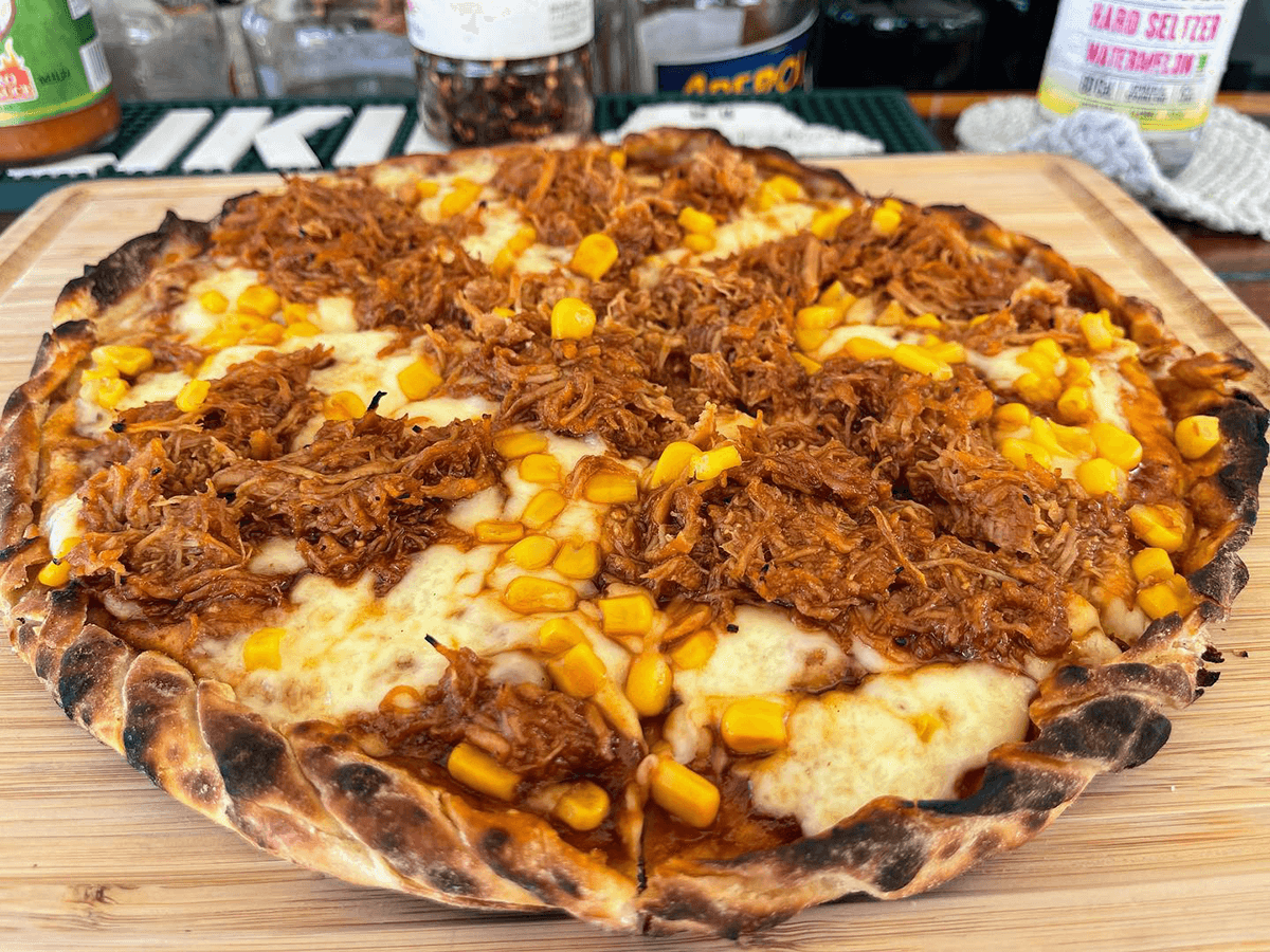 A barbecue chicken pizza topped with shredded meat and corn on a wooden board.