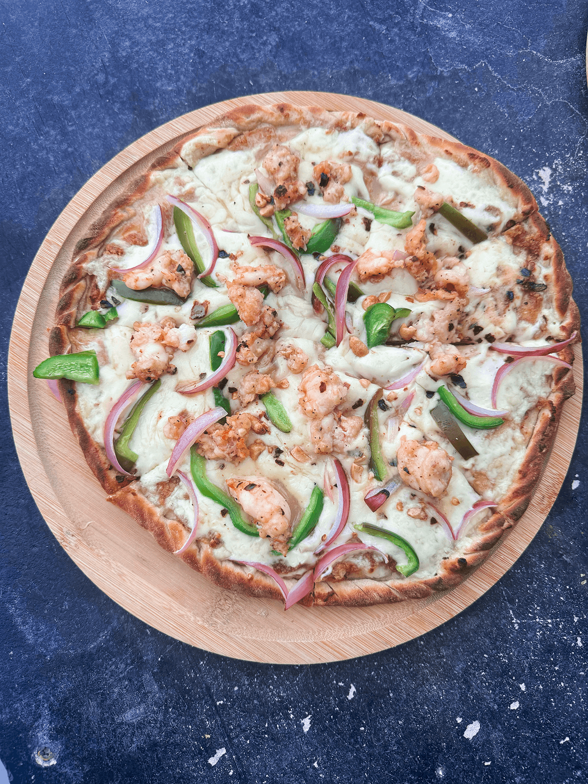 A shrimp pizza topped with green peppers and red onions on a wooden serving board.