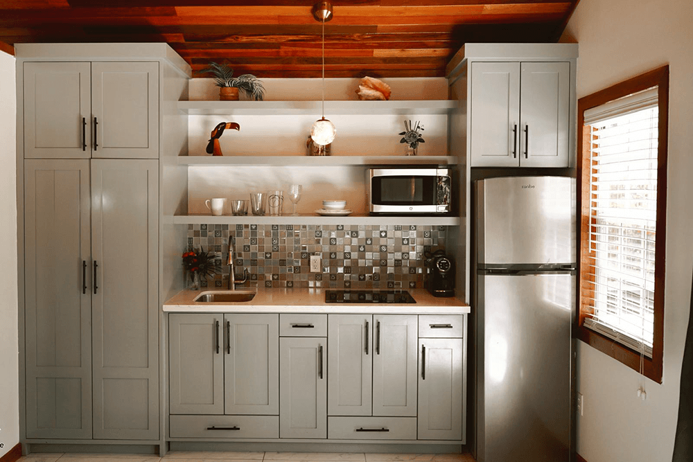 A modern kitchen featuring gray cabinets, a microwave, a stainless steel fridge, and a tiled backsplash.