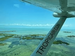 Aerial view of turquoise waters and islands with a plane wing labeled "TROPICAIR.COM" in the foreground.