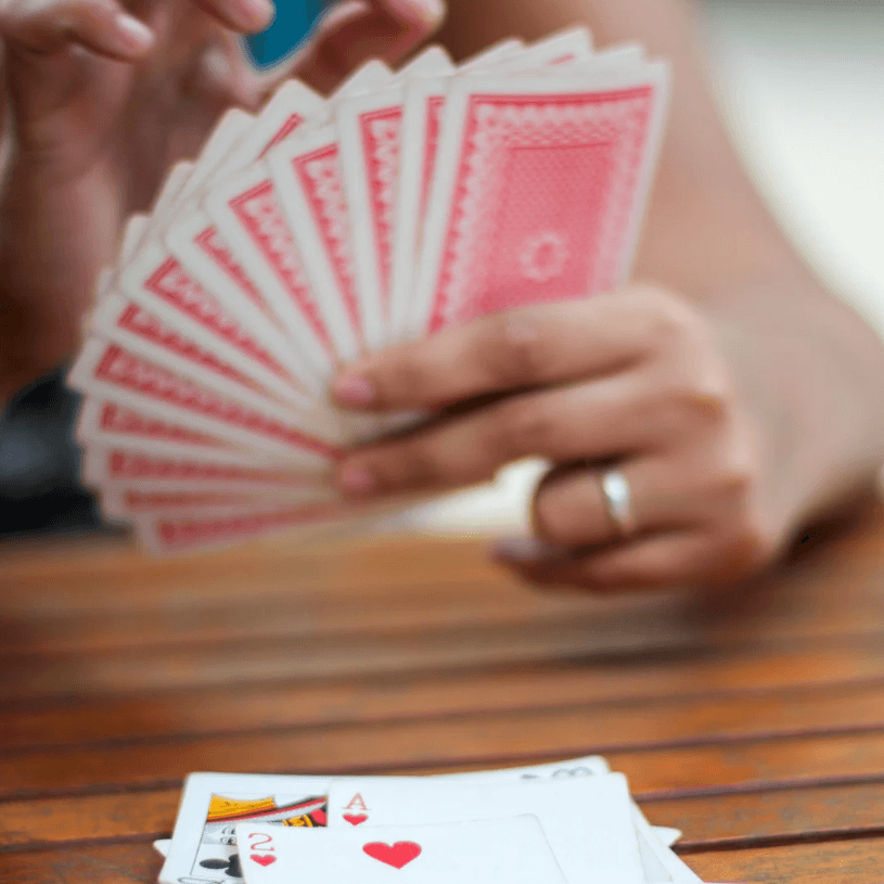 A person holds a fan of red playing cards over a table displaying two visible cards.