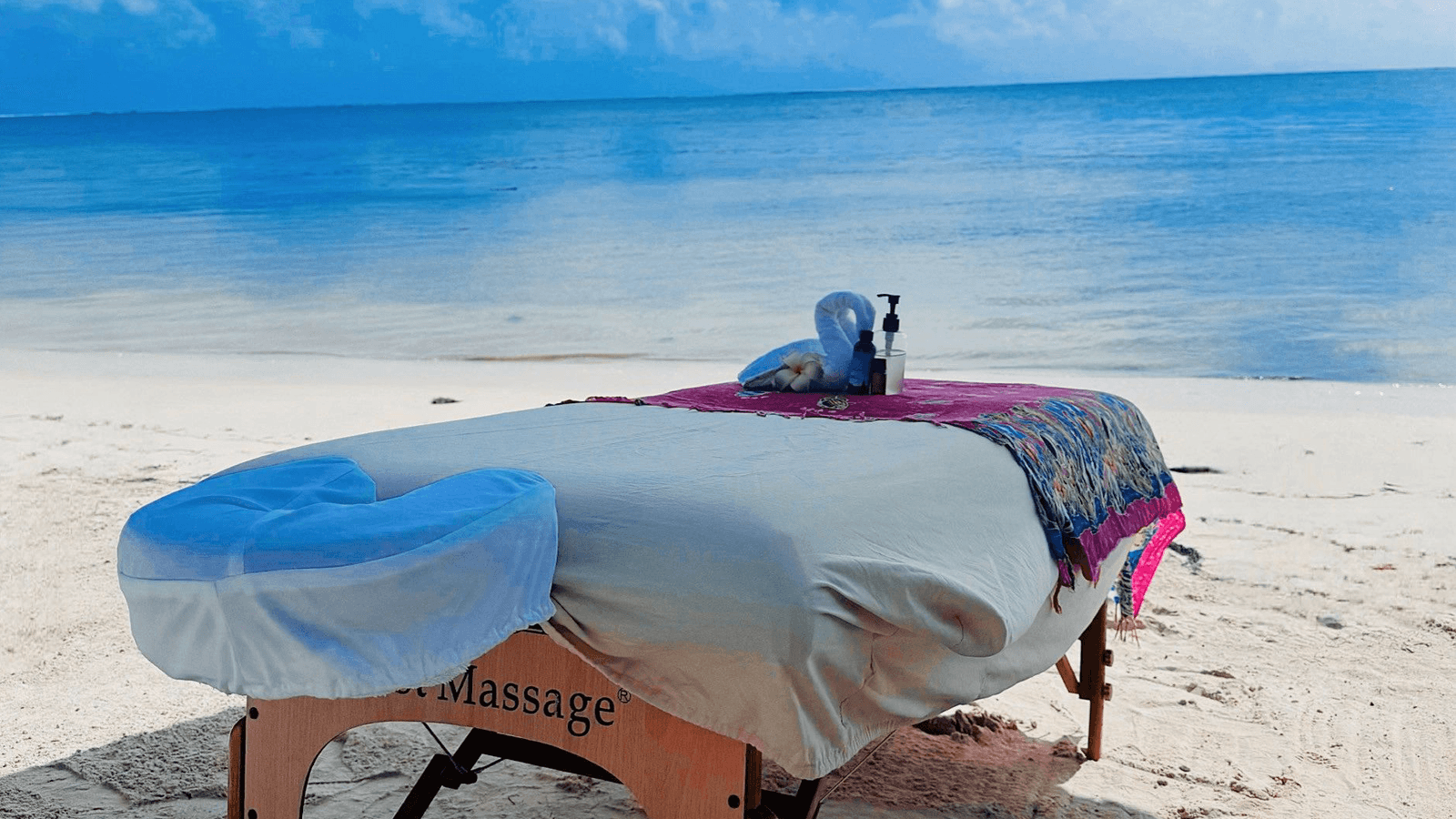 Massage table set up on a sandy beach with calm sea in the background.