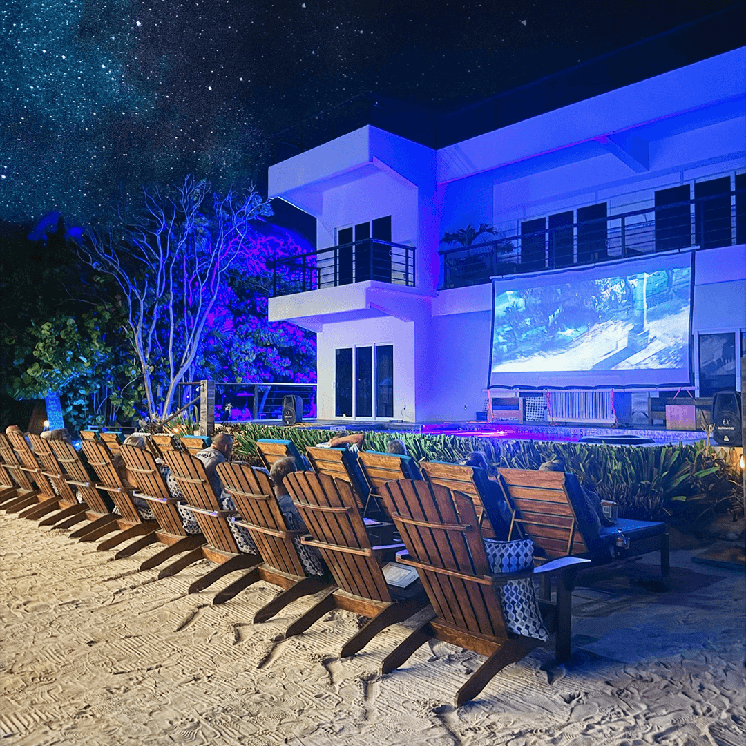 A cozy outdoor movie setup with wooden loungers facing a large screen under a starry night sky.