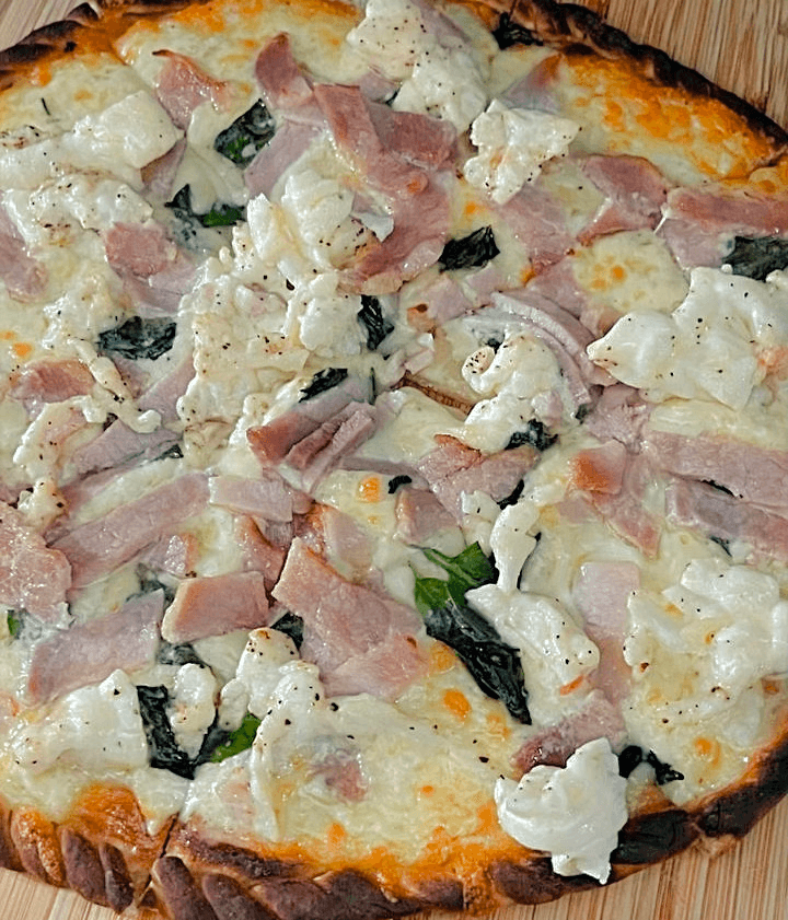 A freshly baked pizza topped with ham, cauliflower, and spinach.