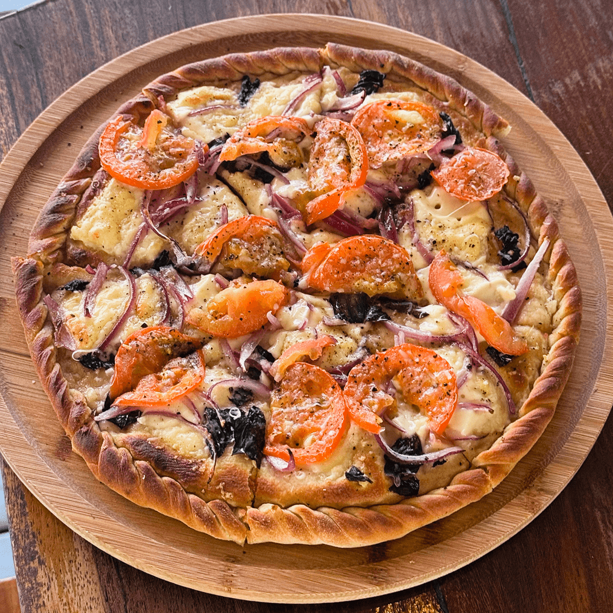 A fresh pizza topped with tomatoes, onions, and herbs, served on a wooden platter.
