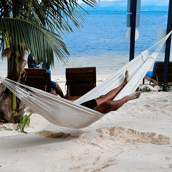 A person relaxes in a hammock by the beach with gentle waves in the background.