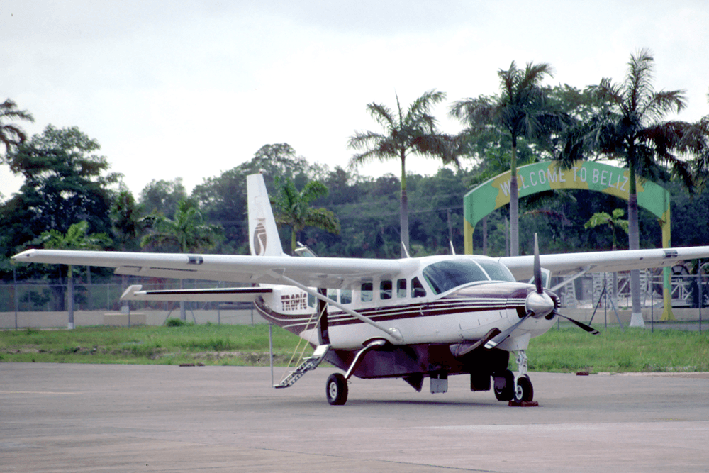 Small airplane parked on a runway with a "Welcome to Belize" sign in the background.