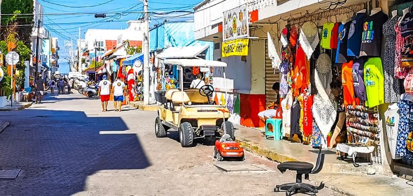 Golf cart parked along a colorful shopping street in San Pedro, Belize, with souvenir shops, pedestrians, and bright storefronts.